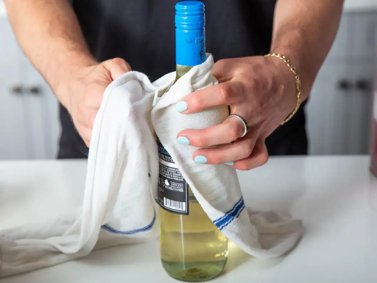 Mani che asciugano una bottiglia di vino bianco con un panno. Quanto tempo può stare il vino bianco in freezer?