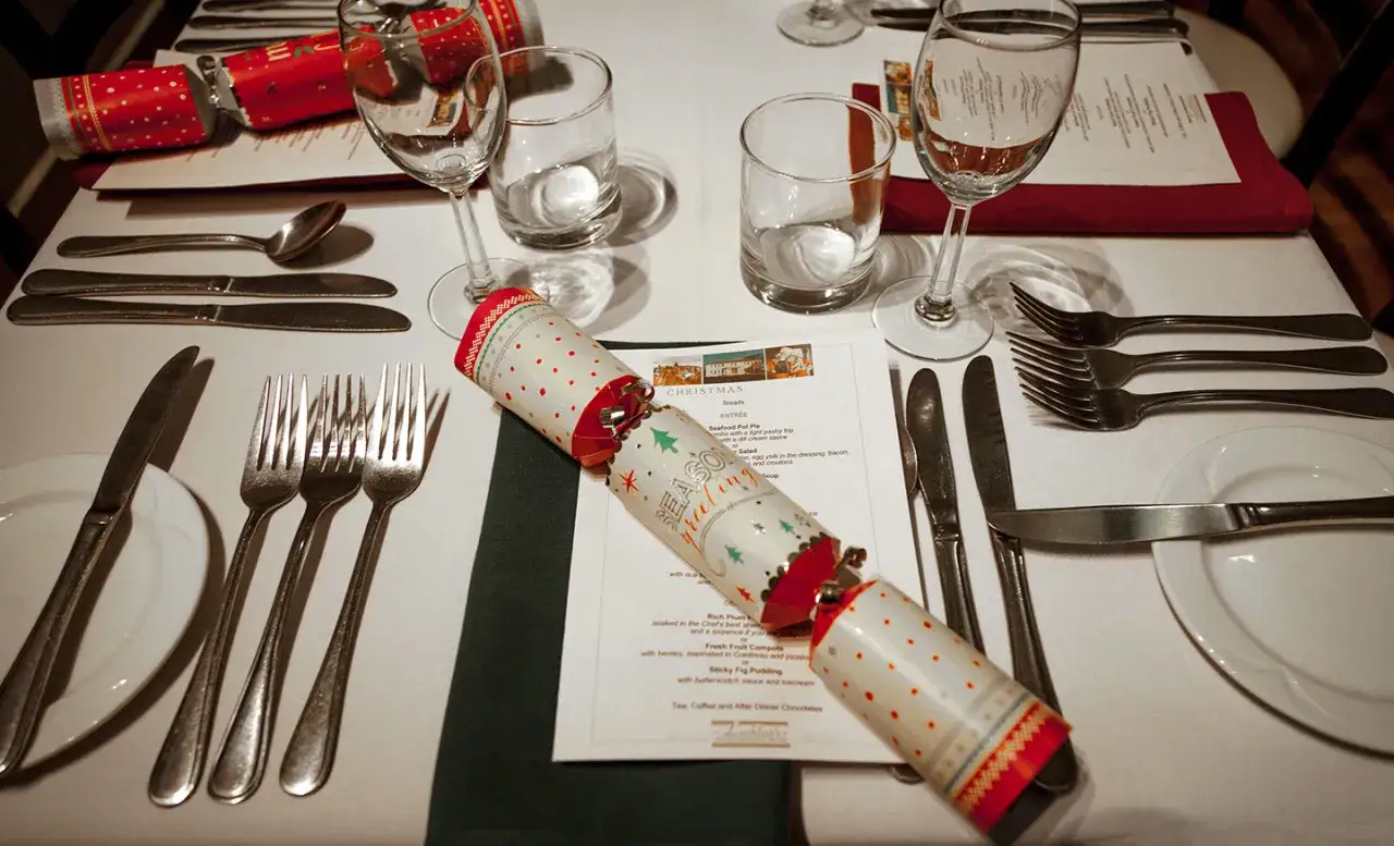 Tavola apparecchiata per le feste, con posate, bicchieri e un cracker natalizio. Chiss&agrave; a chi si versa prima il vino per iniziare questo magico pranzo!