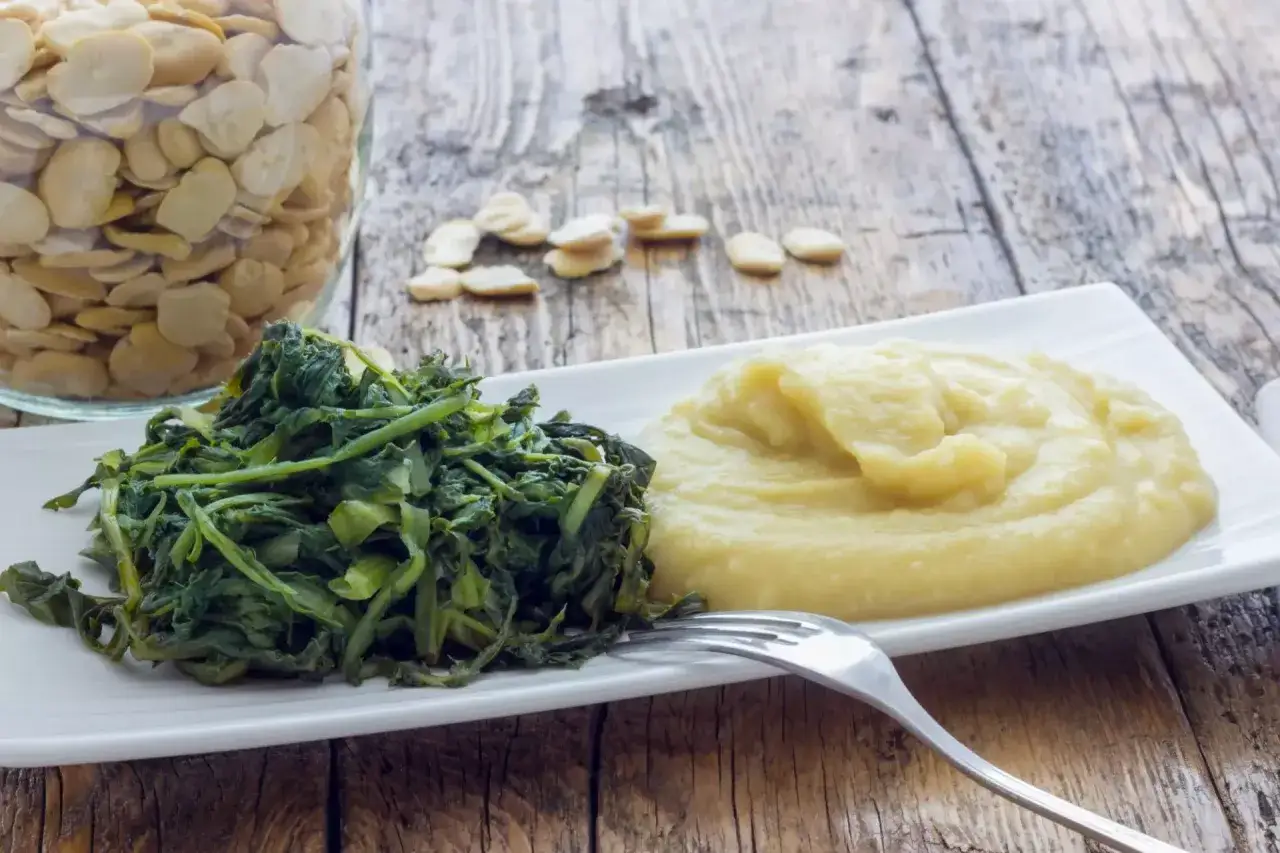 Piatto con verdure verdi e purè di fave, un legume nutriente. Un barattolo di fave secche sullo sfondo.