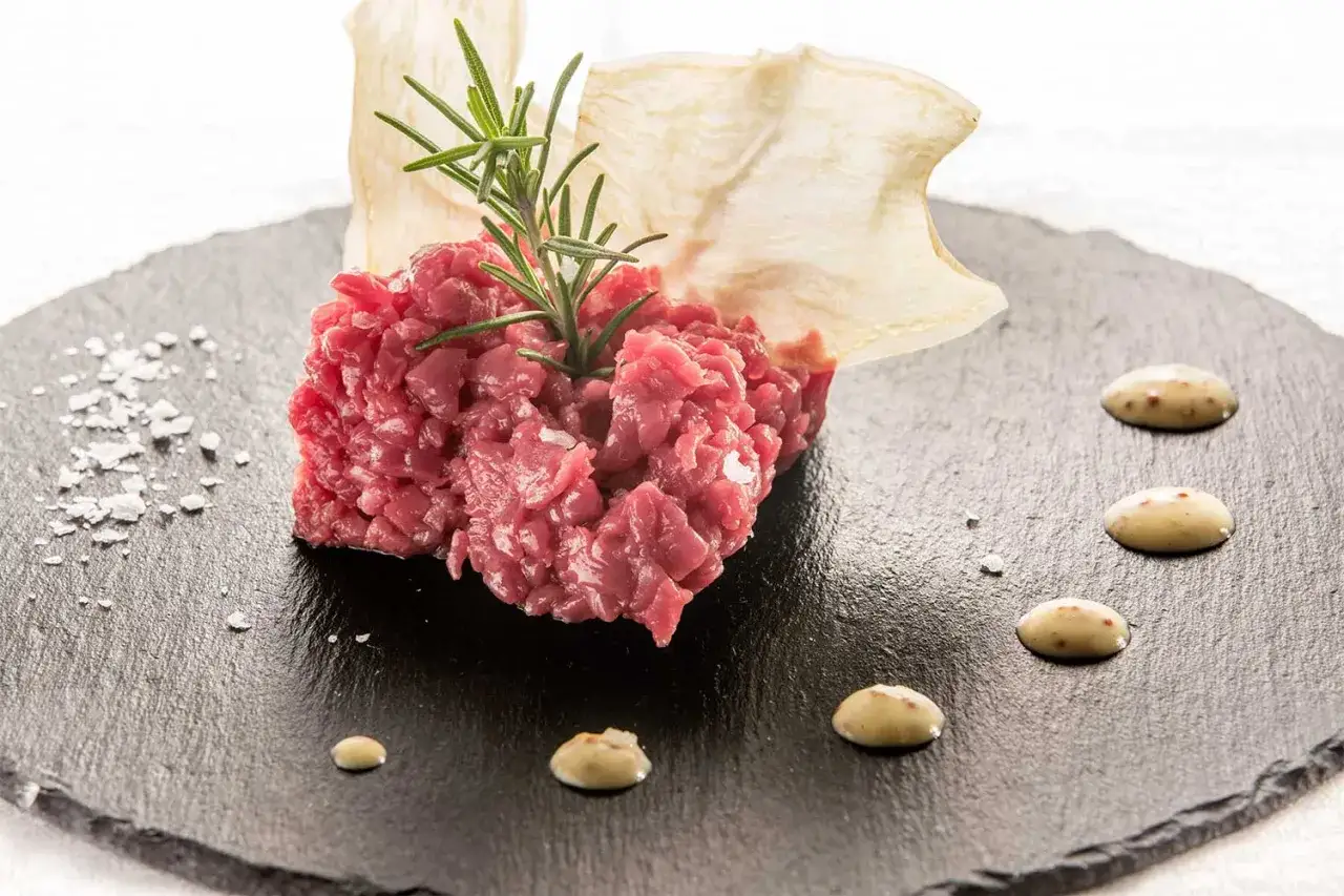 Tartare di manzo su pietra lavica, guarnita con rosmarino e chips croccanti. Perfetta per un abbinamento vino tartare di manzo.