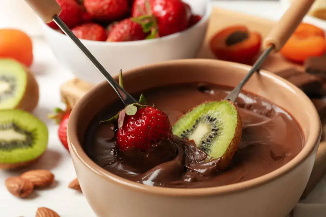 Fragole e kiwi immersi in una fonduta di cioccolato, un delizioso esempio di abbinamenti cioccolato e frutta.