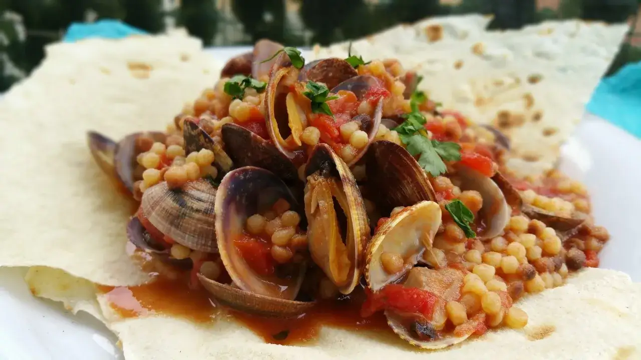 Pasta asciutta con vongole e pomodoro, guarnita con prezzemolo fresco, servita su pane carasau.