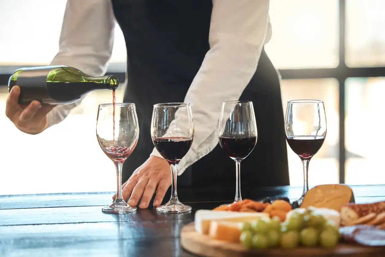 Un sommelier versa vino rosso in quattro bicchieri, pronto per una degustazione.
