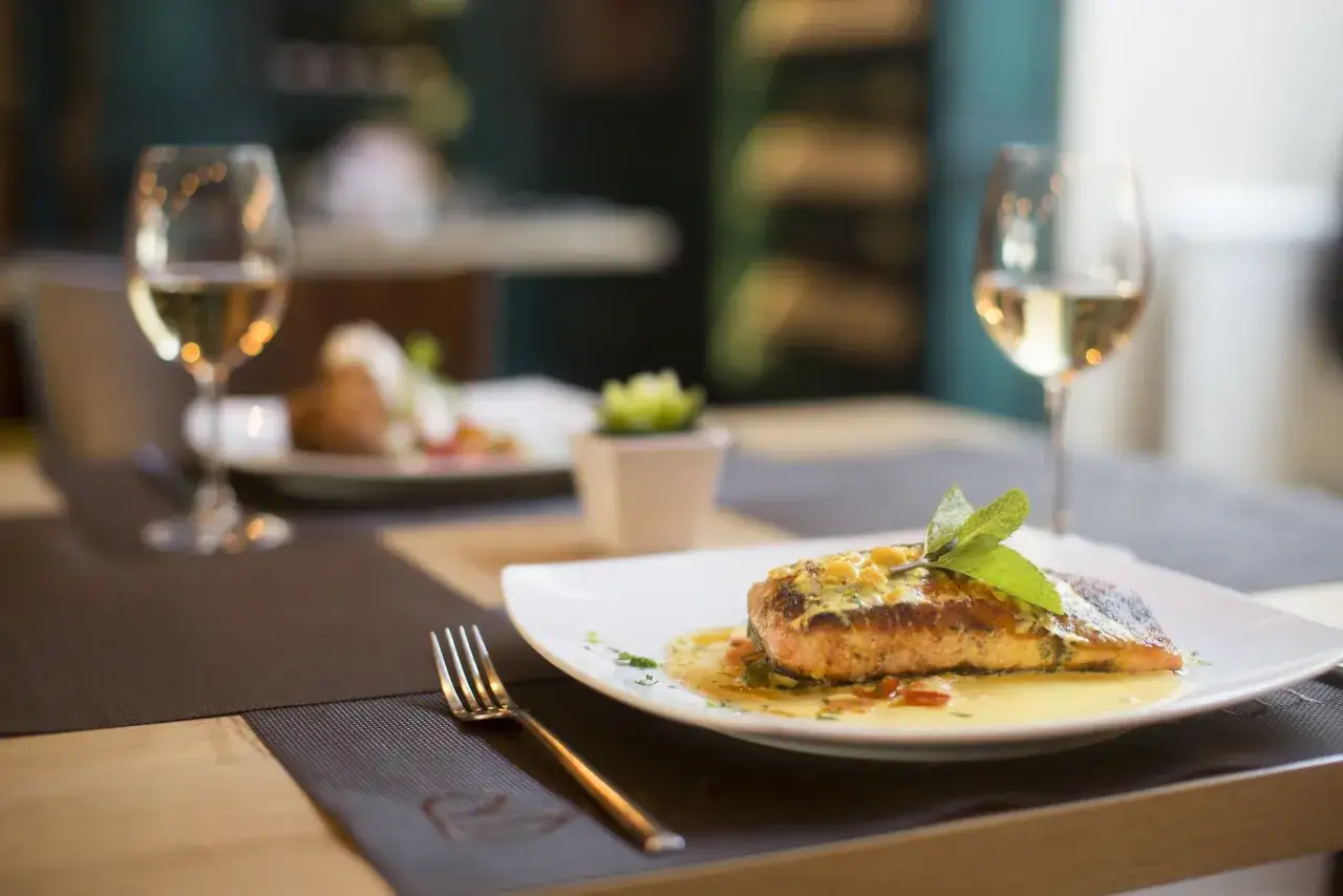 Un succulento filetto di salmone con salsa gialla e menta, servito su un piatto bianco con un bicchiere di vino bianco. Un'idea su cosa abbinare al salmone per un pasto elegante.