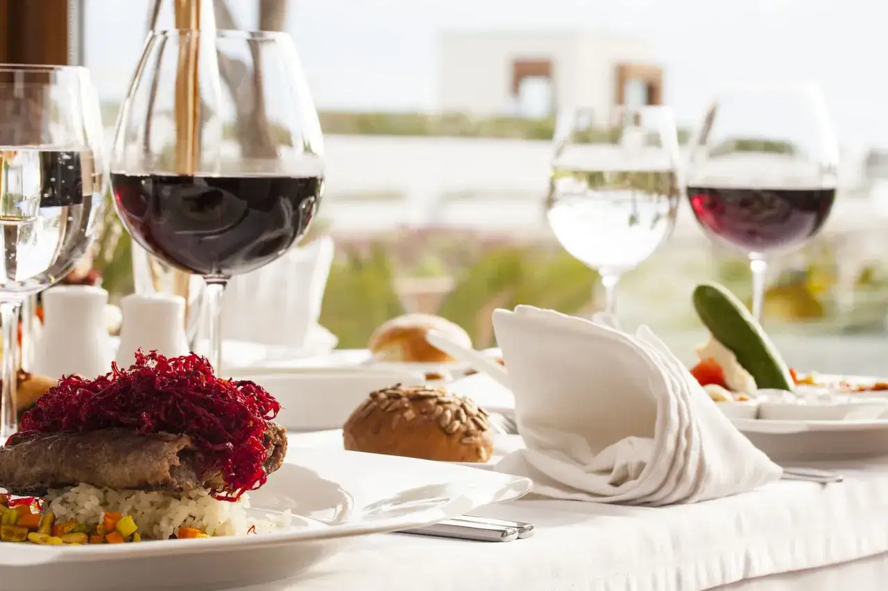 Un piatto raffinato con carne, riso e verdure, accompagnato da vino rosso e acqua. Un perfetto abbinamento cibo vino AIS per una cena elegante.