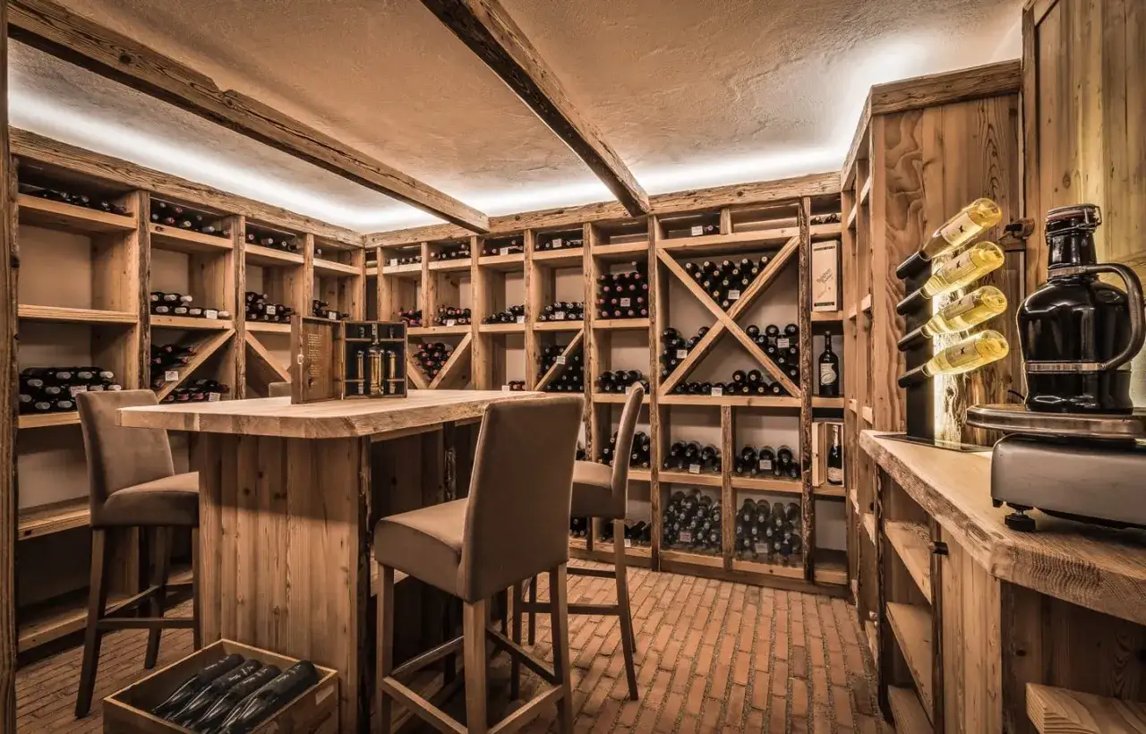 Cantina in legno con scaffali pieni di bottiglie, un bancone e sgabelli. Ideale per chi vuole imparare come fare il vino.