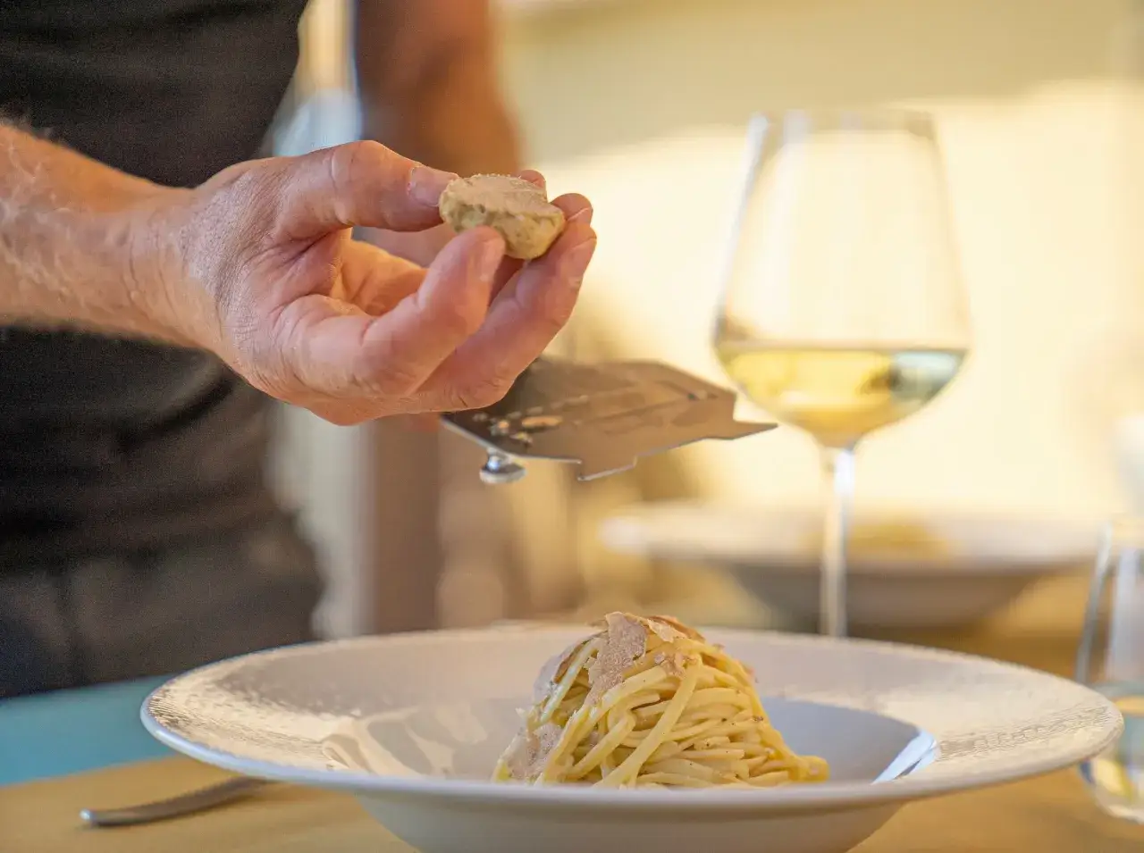Un piatto di spaghetti al tartufo, con una mano che ne grattugia un altro pezzo. Un bicchiere di vino bianco, perfetto per sapere che vino abbinare al tartufo.
