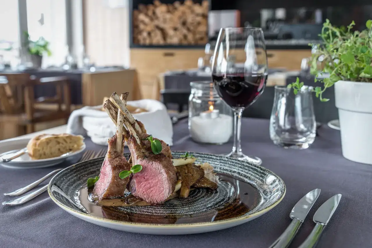 Carr&eacute; d'agnello al forno con funghi e un bicchiere di vino rosso, un abbinamento perfetto per un pasto speciale.
