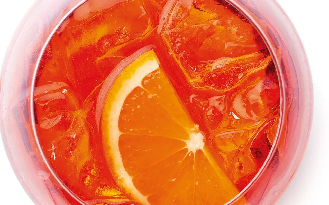 Un bicchiere di Spritz, con ghiaccio e una fetta d'arancia. La ricetta perfetta per un aperitivo rinfrescante.