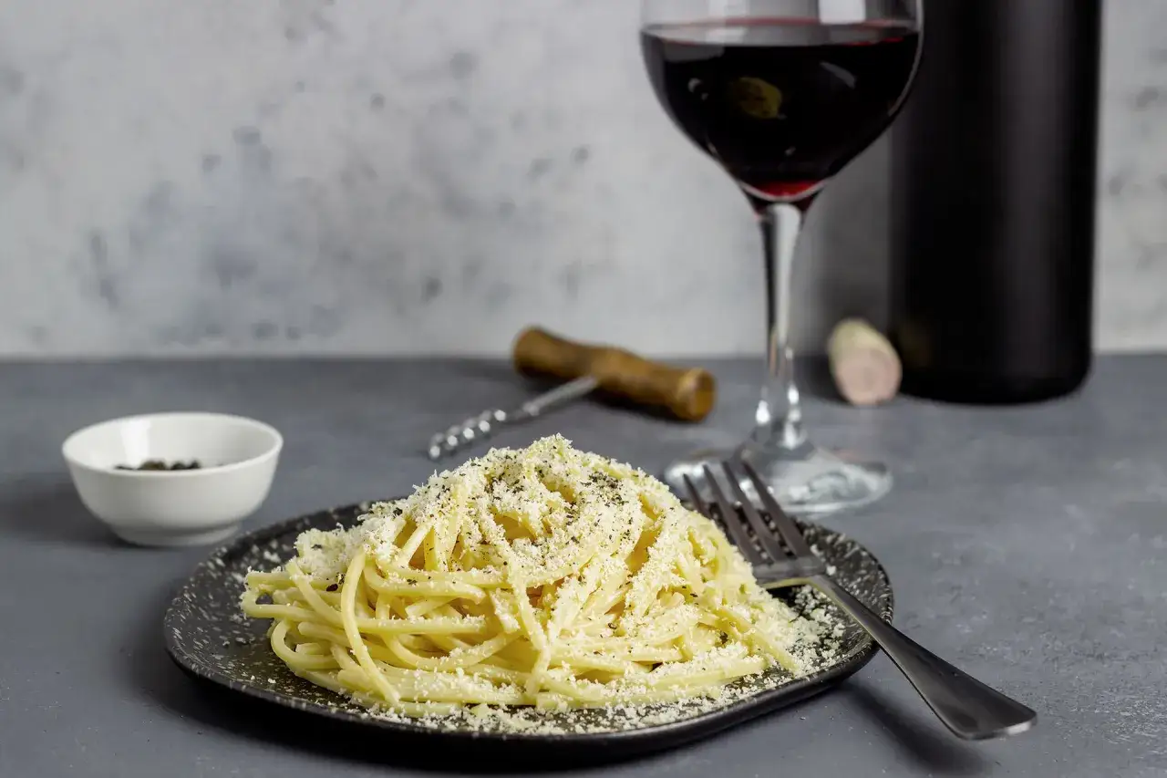Un piatto di spaghetti alla carbonara, un bicchiere di vino rosso e una bottiglia: il perfetto vino per carbonara.