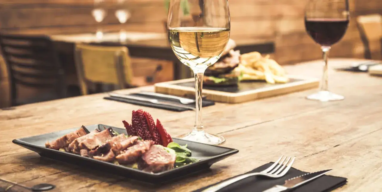 Un bicchiere di vino bianco, perfetto vino bianco per carne alla brace, accompagna un piatto di carne affettata e fragole su un tavolo di legno.