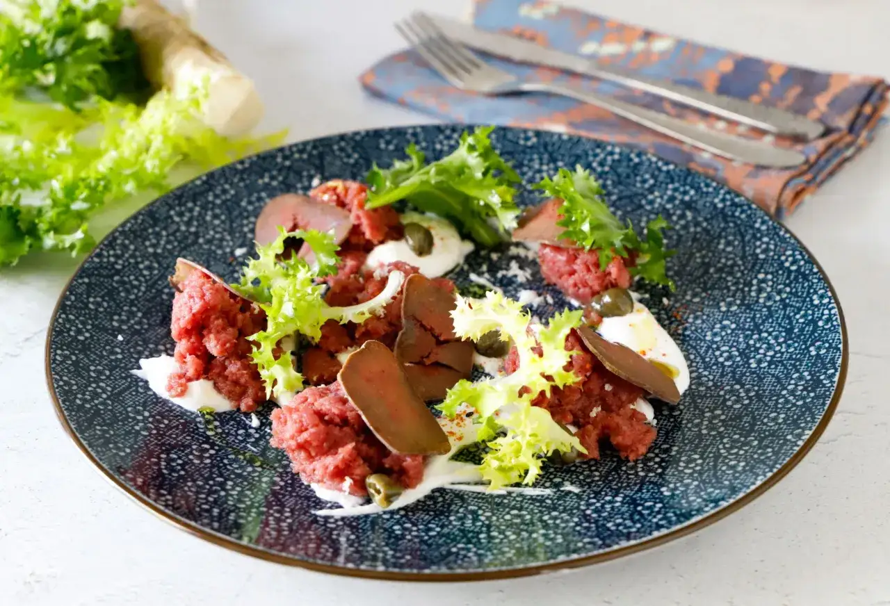 Piatto di carne cruda finemente tritata, guarnito con lattuga croccante, capperi e una salsa bianca.