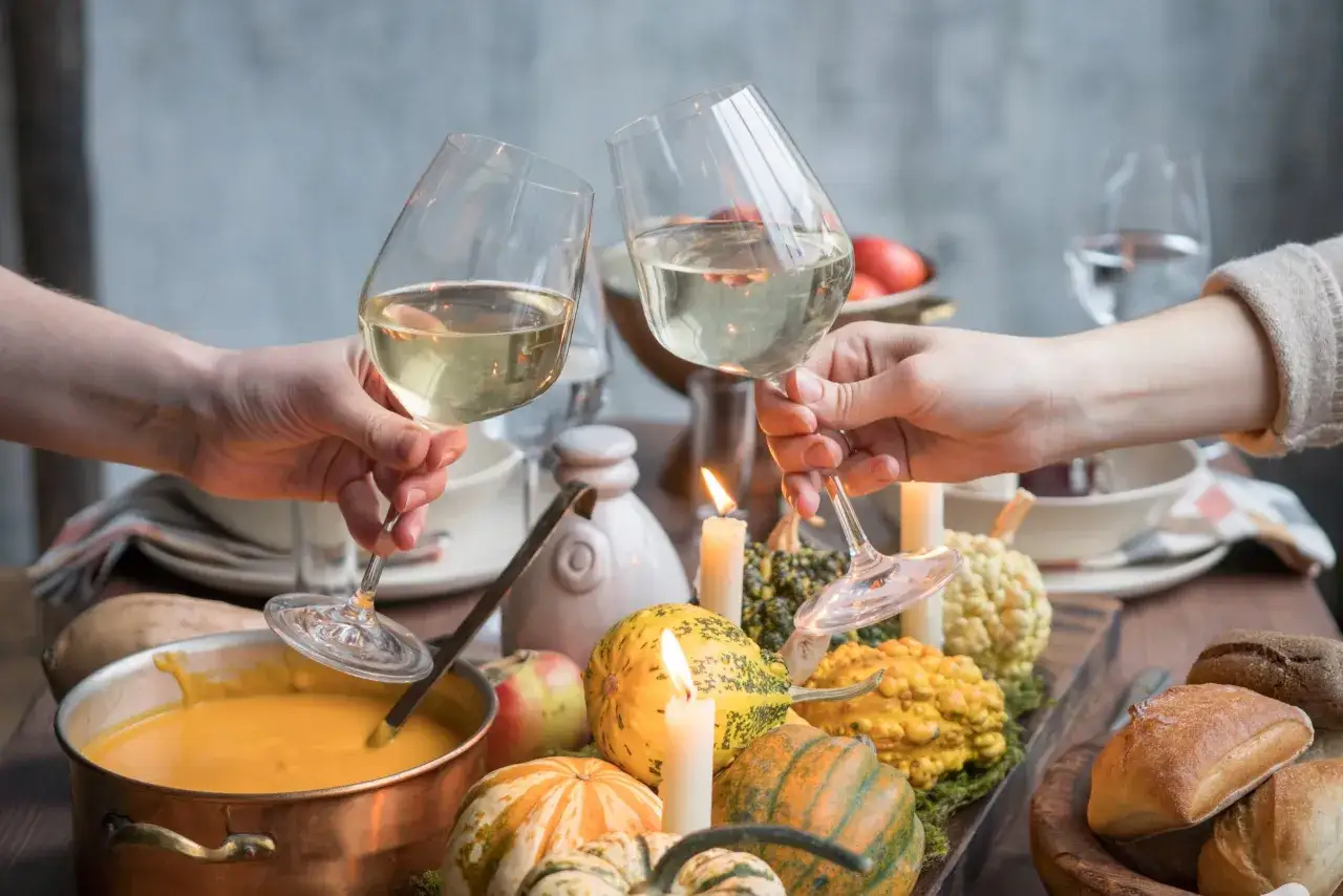 Brindisi con vino bianco su un tavolo autunnale con zucche, crema di zucca e pane. Perfetti abbinamenti con la zucca per una cena speciale.
