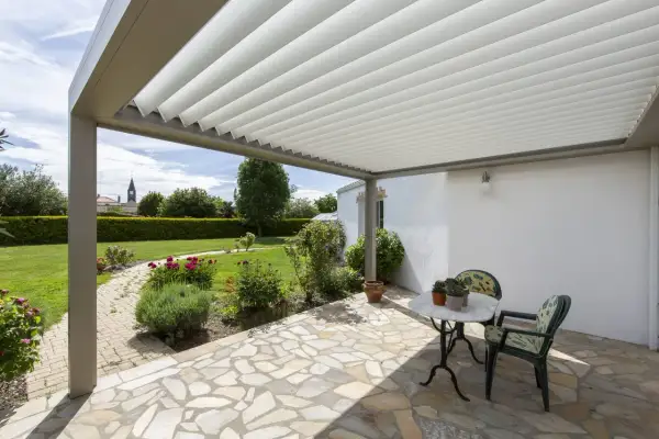 Un angolo relax sotto una vite a pergola semplice, con un tavolino e sedie, affacciato su un giardino fiorito.