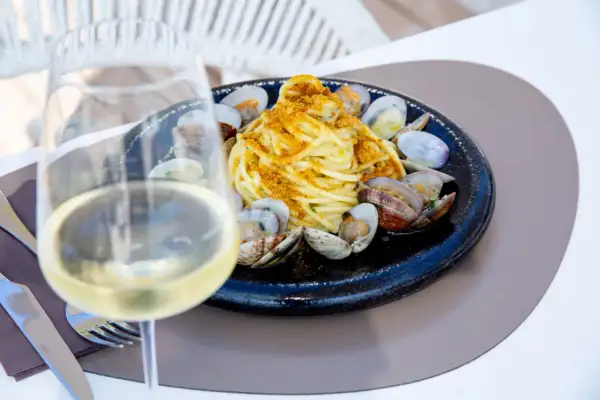 Un bicchiere di vino bianco, perfetto vino bianco da abbinare al pesce, accanto a un piatto di spaghetti alle vongole.