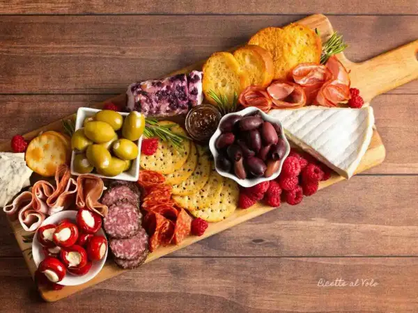 Un invitante tagliere di formaggi misti, salumi, olive, lamponi e crostini, perfetto per un aperitivo.