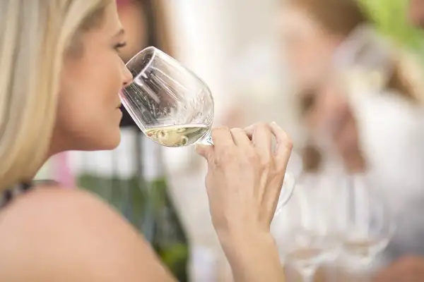 Donna bionda assapora un vino bianco, forse un vino 15 gradi, in un ambiente conviviale.