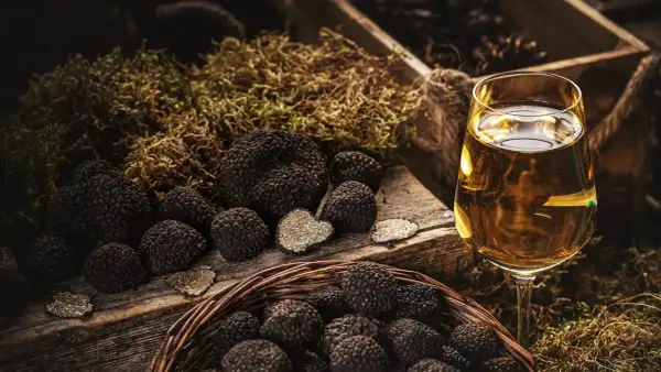 Truffles in a basket and on a wooden board, with a glass of white wine. La domanda è: che vino abbinare al tartufo?