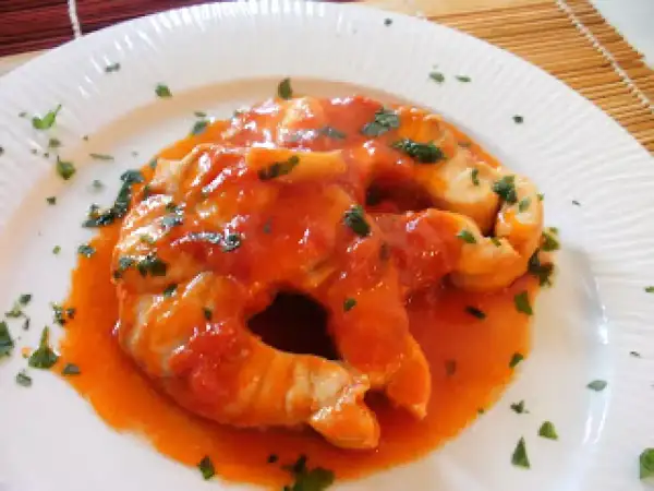 Due fette di pesce palombo cotte in salsa di pomodoro e guarnite con prezzemolo tritato, servite su un piatto bianco.