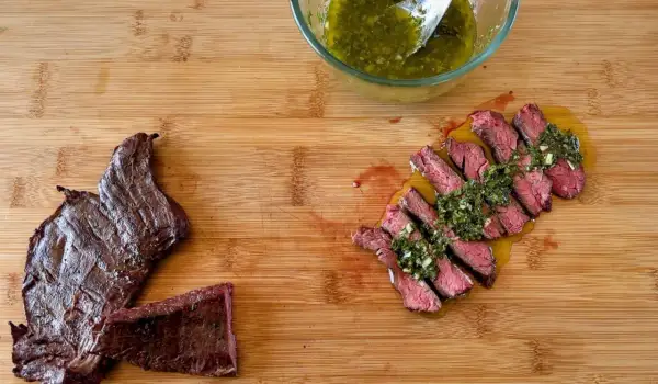 Fetta di manzo che carne è, succulenta e affettata, condita con salsa verde su tagliere di legno.