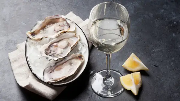 Un piatto di ostriche fresche su ghiaccio, accompagnato da un bicchiere di vino bianco frizzante e spicchi di limone. Un'elegante degustazione di ostriche e vino.