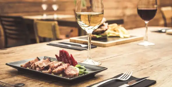 Un bicchiere di vino bianco, perfetto vino bianco per carne alla brace, accanto a un piatto di carne affettata e fragole su un tavolo di legno.
