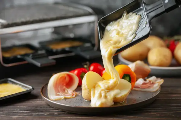 Formaggio fuso che cola su patate e salumi, un delizioso esempio di diversi tipi di formaggio usati per la raclette.