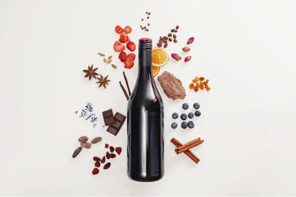 Bottiglia di vino rosso con ingredienti: fragole, arancia, mirtilli, cioccolato, cannella, anice stellato, caffè, bacche di ginepro e scorza d'albero, che suggeriscono note di tannino gallico.