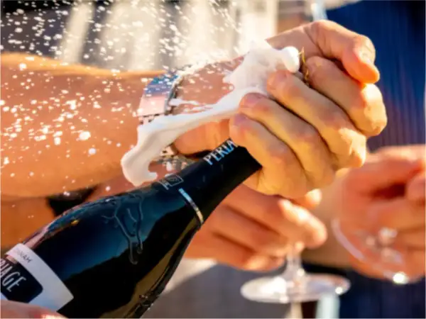 Le mani aprono una bottiglia di spumante, la schiuma esplode. La pressione della bottiglia spumante è alta, pronta per festeggiare.