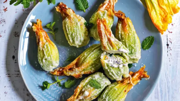 Fiori di zucca fritti, ripieni di formaggio cremoso e guarniti con menta fresca, su un piatto blu.