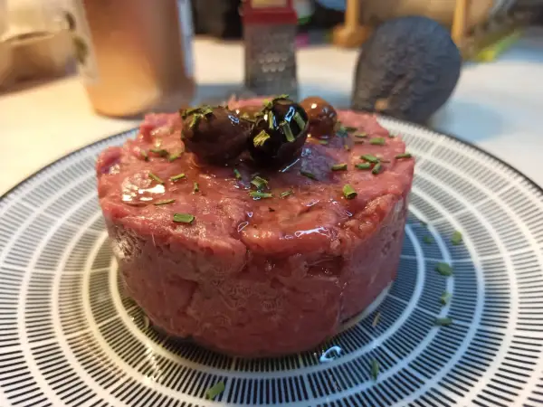 Un delizioso tartare di carne cruda, guarnito con olive nere e erba cipollina, pronto per essere gustato.