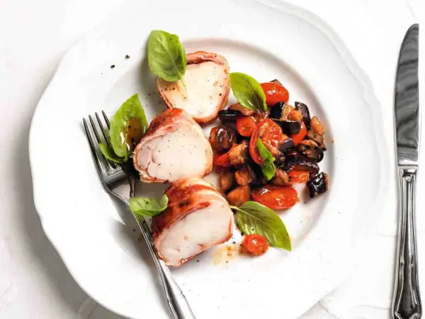 Tranci di rana pescatrice avvolti nel prosciutto, serviti con ratatouille di verdure e basilico fresco.