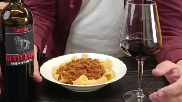 Un bicchiere di vino rosso e un piatto di pasta al ragù, accompagnati da una bottiglia di Gutturnio.