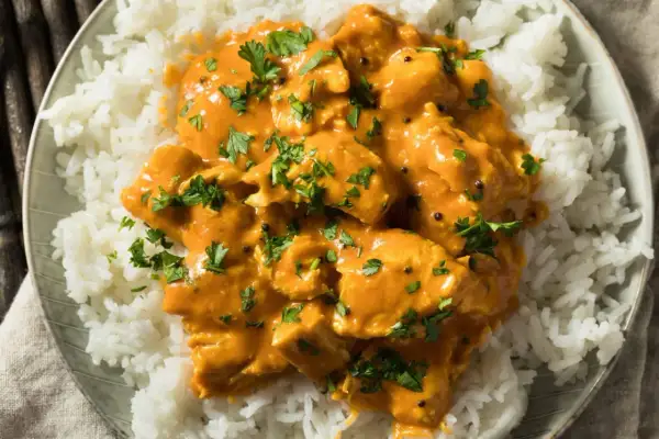 Piatto di riso bianco con pollo al curry arancione, guarnito con prezzemolo fresco. Perfetto con vino bianco o rosso.