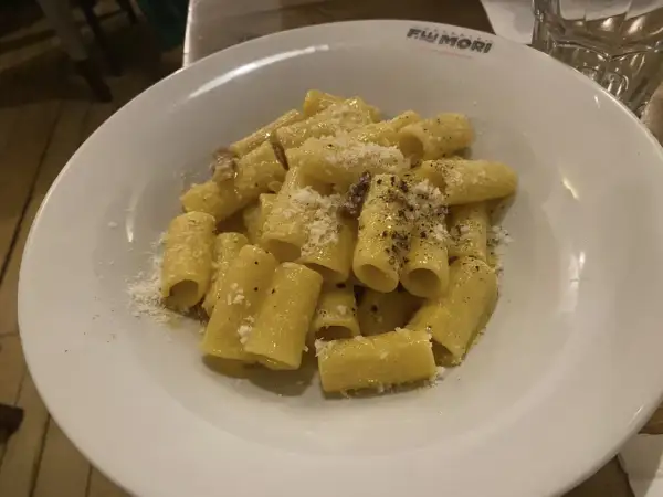 Piatto di rigatoni alla carbonara, conditi con guanciale croccante, pecorino romano e pepe nero. Perfetto con un bicchiere di vino bianco secco.